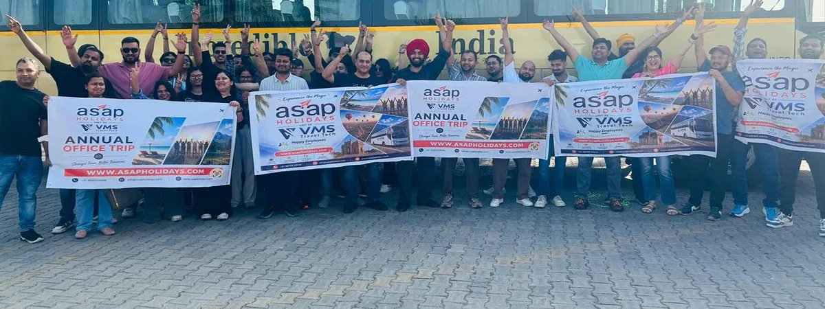 The whole team holding Annual Office Trip banners in front of the coach