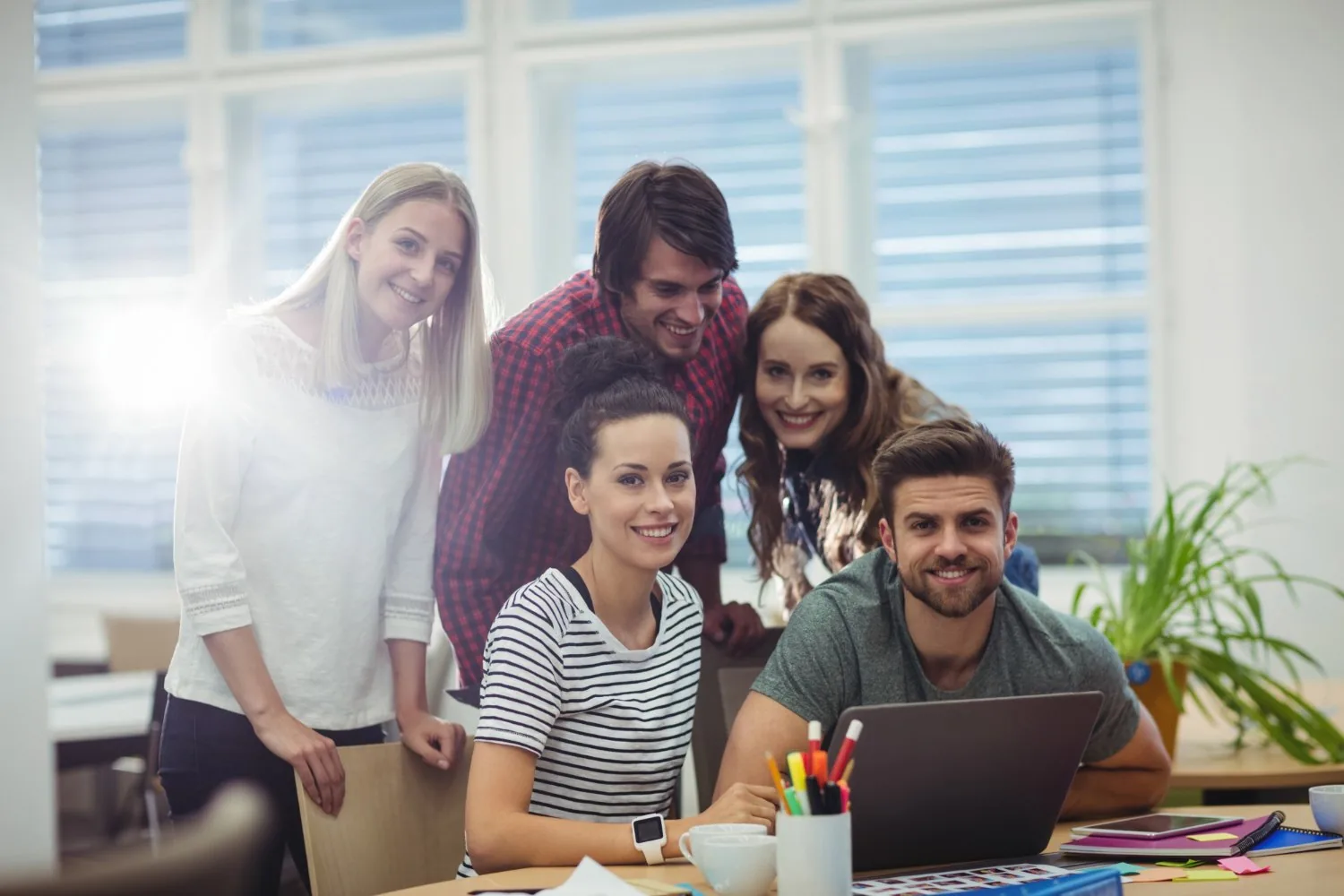 A smiling customer support team gathered around a laptop