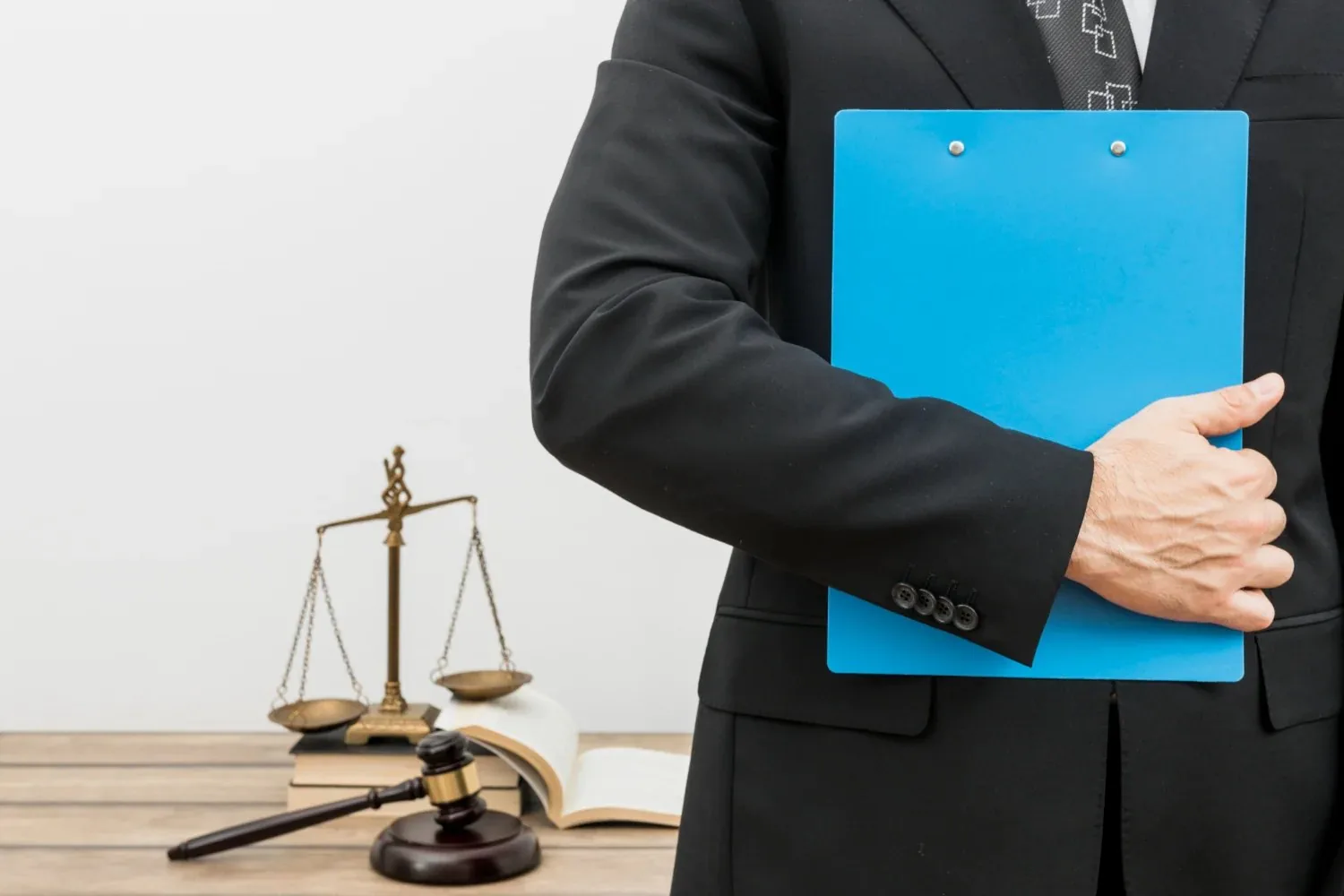 A lawyer holding a blue case folder beside the scales of justice and a gavel